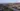 © Kapsch TrafficCom Luftaufnahme einer Autobahn in einer Stadt mit umgebenden Gebäuden und Bergen im Hintergrund.
